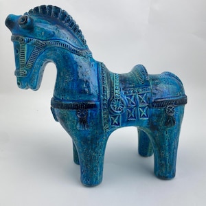 May include: A turquoise ceramic horse figurine with detailed saddle and bridle. The horse has a textured surface and stands on four legs. This decorative figurine is a unique item.