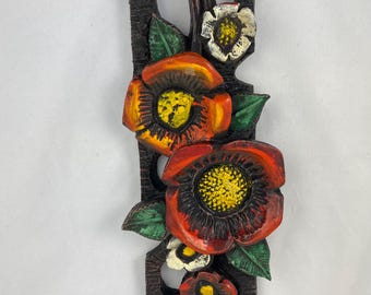 Könnte beinhalten: Ein Wandbehang aus Holz mit einem geschnitzten Design aus roten, orangefarbenen und weißen Blumen. Die Blumen sind realistisch bemalt und haben grüne Blätter.