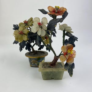 Op de afbeelding: Twee miniatuur bonsai-bomen met kleurrijke, doorschijnende bloemen en donkergroene bladeren. Eén boom staat in een vierkante, lichtgroene pot, de andere in een ronde, blauw en gouden pot. De bloemen zijn in tinten geel, oranje en wit.