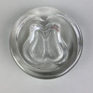 Op de afbeelding: Transparante glazen asbak met een cirkelvormig ontwerp. De asbak heeft een centrale verdieping met een dubbel peer-vormig ontwerp. De rand van de asbak is afgerond en glad.