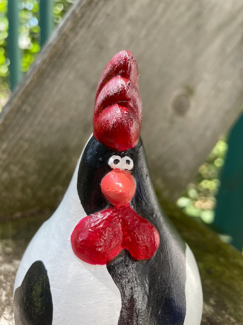 May include: A hand-painted ceramic chicken figurine with black and white spots and a red comb. The chicken has a whimsical expression with large eyes and a red beak.