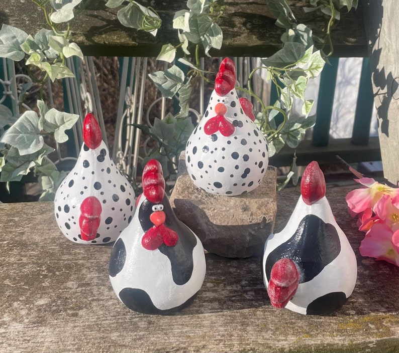 May include: Four ceramic chicken figurines with black and white polka dot patterns and red accents. The chickens are standing on a wooden surface.