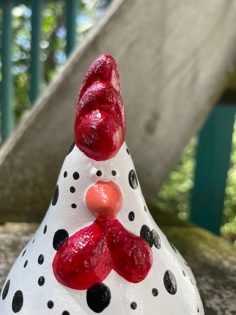 May include: A white ceramic chicken figurine with black polka dots. The chicken has a red comb and wattle, and a pink beak.