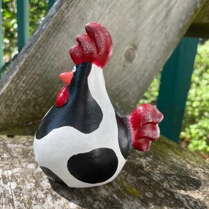 May include: A black and white ceramic rooster figurine with red accents. The rooster has a cow-like pattern with black spots on a white background.