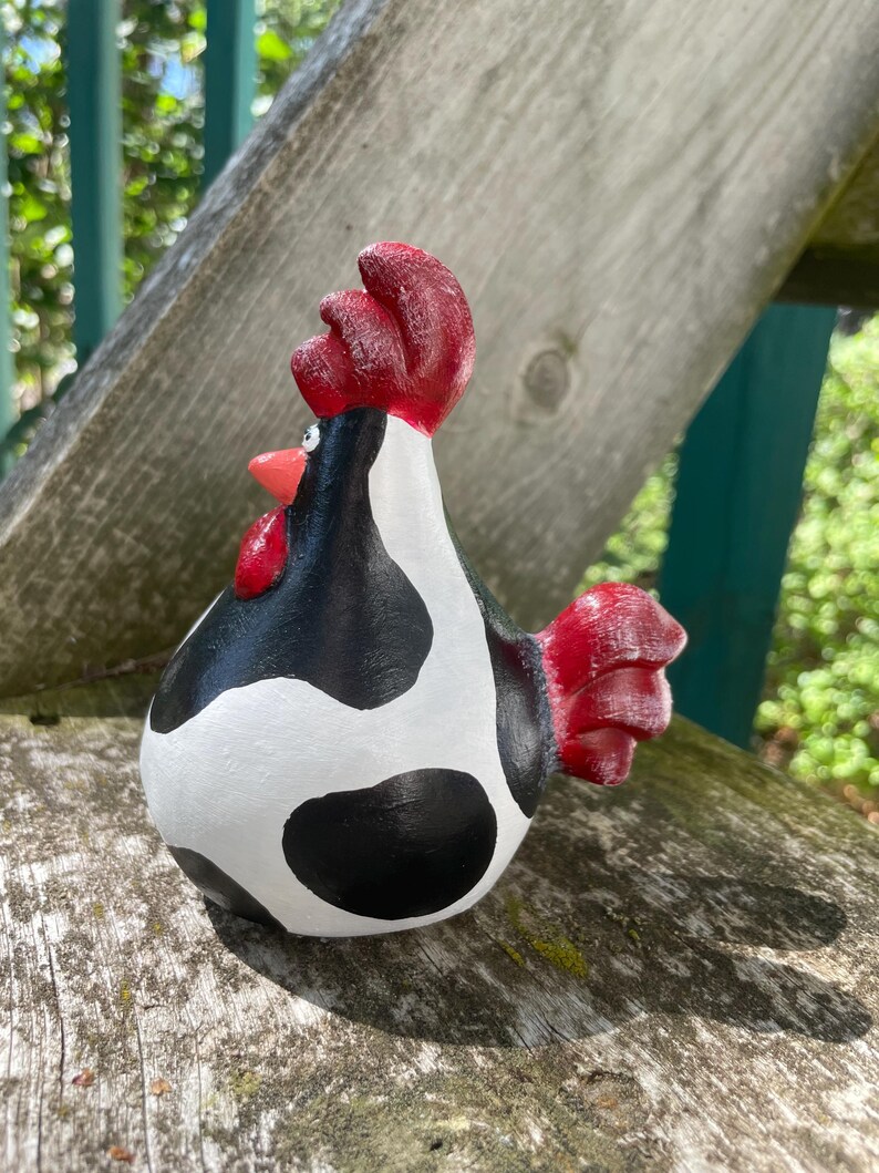 May include: A black and white ceramic rooster figurine with red accents. The rooster has a cow-like pattern with black spots on a white background.