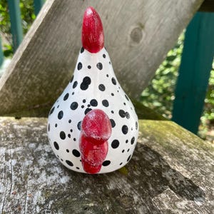 May include: A white ceramic chicken figurine with black polka dots and a red comb. The chicken is sitting on a wooden surface.