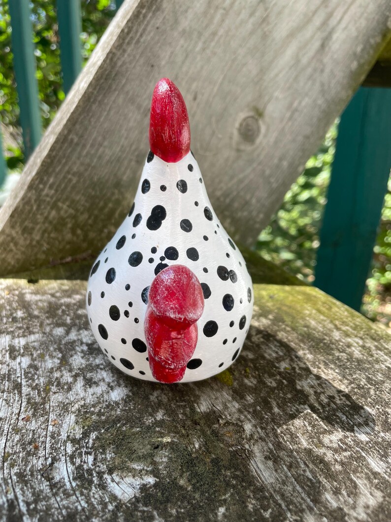 May include: A white ceramic chicken figurine with black polka dots and a red comb. The chicken is sitting on a wooden surface.