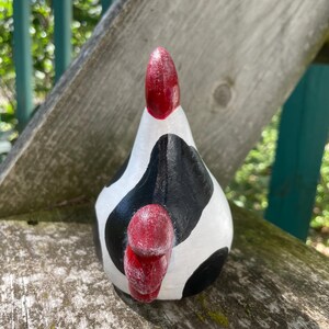 May include: A white and black ceramic chicken figurine with red accents. The chicken is painted to look like a cow with black and white spots.