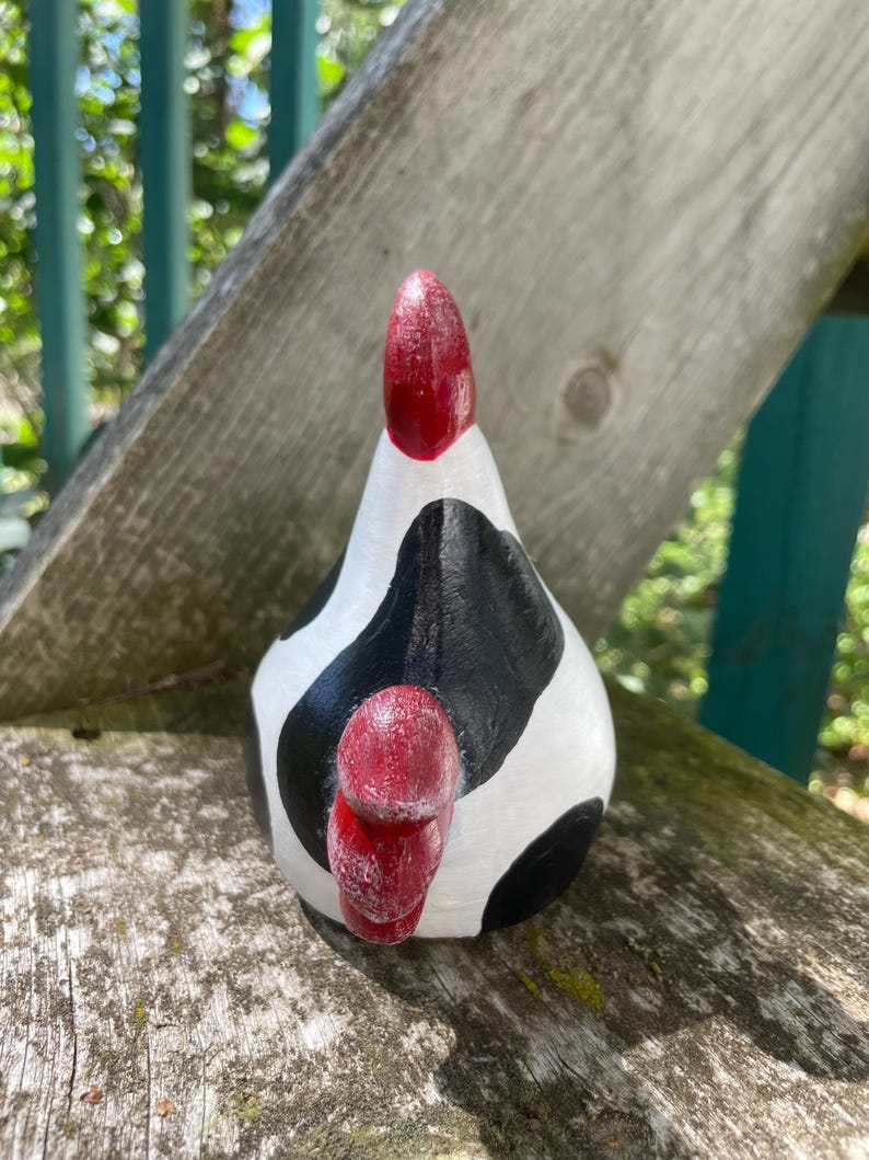 May include: A white and black ceramic chicken figurine with red accents. The chicken is painted to look like a cow with black and white spots.