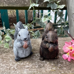 Puede incluir: Dos figuritas de ardilla grises y marrones que sostienen nueces en sus patas. Las ardillas están sentadas sobre una superficie de madera.