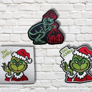 Op de afbeelding: Drie geborduurde patches met de Grinch met een kerstmuts. Eén patch toont de Grinch met een zak cadeaus, terwijl de andere twee de Grinch tonen met de tekst "Bah Humbug". De patches zijn groen, rood en wit.