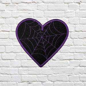 May include: A heart-shaped patch with a black background and a purple spiderweb design. The patch has a purple border and is set against a white brick wall. This patch is suitable for Halloween or gothic-themed projects.