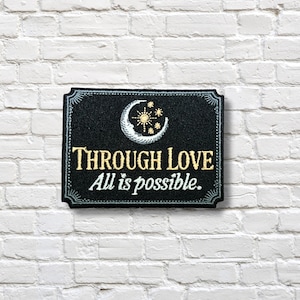 Puede incluir: Parche rectangular negro con borde decorativo. El parche presenta un diseño de luna creciente, estrellas y sol. El texto "THROUGH LOVE" y "All is possible." están bordados en oro y blanco.