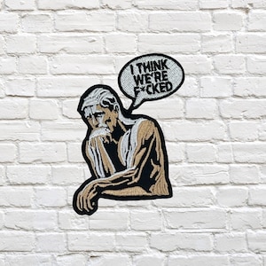 May include: Embroidered patch featuring a contemplative figure with the text "I THINK WE'RE F*CKED" in a speech bubble. The patch has a black border, with tan and black details, and is set against a white brick wall.