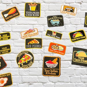 以下が含まれることがあります： さまざまな食べ物をテーマにした刺繍パッチのコレクション。フライドチキン、ピザ、タコス、シャワルマ、ブランチ、カレー、インド料理などのデザイン。各パッチにはテキストが記載されています。