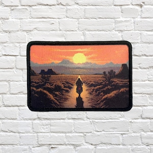 Può includere: Toppa rettangolare con una scena di tramonto nel deserto. Un motociclista solitario percorre una strada verso il sole al tramonto. Il cielo è un gradiente di arancione e giallo. La toppa ha un bordo nero.