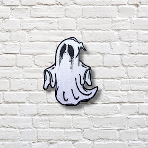 Puede incluir: Parche de fantasma blanco con detalles en negro. El fantasma tiene ojos negros y marcas en forma de lágrimas. El parche está delineado en negro y está diseñado para aplicarse en ropa o accesorios.