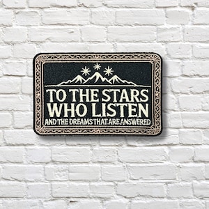 May include: Black rectangular patch with the text "TO THE STARS WHO LISTEN AND THE DREAMS THAT ARE ANSWERED" in white. The patch features a mountain range and stars design. The border is a decorative beige pattern.