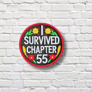 May include: A round, black patch with a red border and the text "I SURVIVED CHAPTER 55" in white. The patch is decorated with yellow and red floral accents and green leaves. The patch is set against a white brick wall.