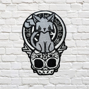 May include: Black and white embroidered patch featuring a cat with a skull and a clock face. The cat is sitting on top of the skull, and the clock face is behind the cat.