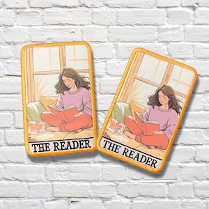 May include: Two rectangular patches with a yellow border. Each patch features an illustration of a person reading a book, with a cat nearby. The text "THE READER" is at the bottom. The person is wearing a pink sweater and orange pants.