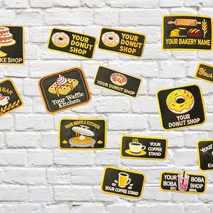 May include: A selection of black and yellow patches with food-themed designs. The patches depict donuts, waffles, cakes, coffee cups, and boba drinks, with text including "Your Donut Shop" and "Your Boba Shop". The patches are on a white brick wall.