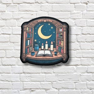 May include: Embroidered patch featuring a nighttime library scene. The design includes bookshelves, a crescent moon, stars, candles, and an open book. The color palette consists of blues, yellows, and browns, creating a cozy, whimsical aesthetic.