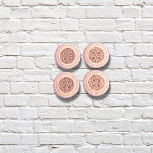 May include: Four round buttons arranged in a square formation. Each button features a light pink outer rim and a textured, darker pink centre with four holes. The surface of each button displays a detailed, intricate pattern of small, raised dots.