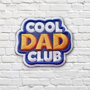 Pode incluir: Patch bordado com as palavras "COOL DAD CLUB" em letras brancas e laranja sobre um fundo azul. O patch é contornado em azul e preto e é colocado contra uma parede de tijolos brancos.