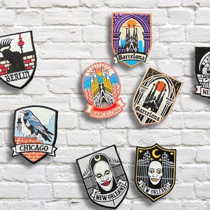 May include: Embroidered patches with city and landmark designs, including Berlin, Barcelona, New York, Chicago, and New Orleans. The patches display iconic imagery and text on a white brick background.