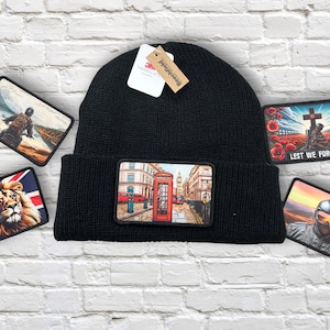 Op de afbeelding: Zwarte gebreide beanie met een rechthoekige patch met een Londense scène met een rode telefooncel. Extra patches tonen een leeuw, een motorrijder, een oorlogsmonument met de tekst "Lest We Forget" en een motorrijder.