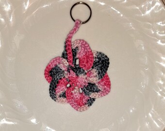 May include: A pink, grey, and white crocheted flower keyring with a silver ring.