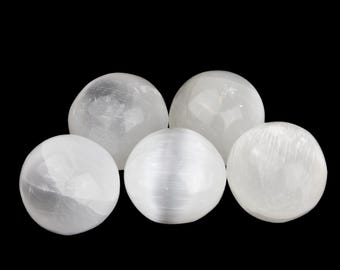 Op de afbeelding: Vijf witte selenietbollen van verschillende grootte zijn geplaatst tegen een zwarte achtergrond. De bollen hebben een doorschijnend, kristallijn uiterlijk, met zichtbare interne structuren. De belichting benadrukt de natuurlijke texturen en vormen van de stenen.