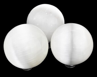 Op de afbeelding: Drie witte seleniet bollen van verschillende grootte zijn geplaatst tegen een zwarte achtergrond. De bollen hebben een glad, gepolijst uiterlijk, met subtiele interne strepen zichtbaar op het oppervlak. Het algehele effect is er een van eenvoudige elegantie.