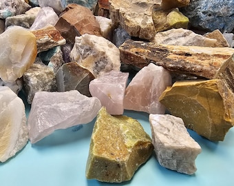 Puede incluir: Una colección de piedras preciosas en bruto de varios colores, incluyendo rosa, verde, marrón y blanco. Las piedras tienen texturas rugosas y naturales, y tamaños variados. La imagen está bien iluminada, mostrando los detalles de cada piedra.
