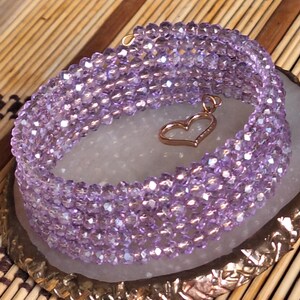 May include: A purple crystal beaded bracelet with a gold heart charm. The bracelet is made of many small, faceted beads that are strung together in a woven pattern.