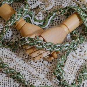 May include: A green and white braided rope with leaves woven into the design. The rope is wrapped around two wooden hands.
