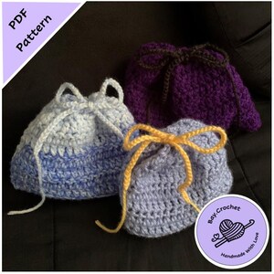 May include: Three crocheted drawstring bags in shades of blue, purple, and gray. Each bag has a contrasting drawstring closure. The bags are handmade and feature the text "PDF Pattern" and a logo that says "Bay.Crochet Handmade With Love."