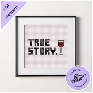May include: A framed cross-stitch design with the text "TRUE STORY." and a glass of red wine. The design is on a pink background and is framed in black.