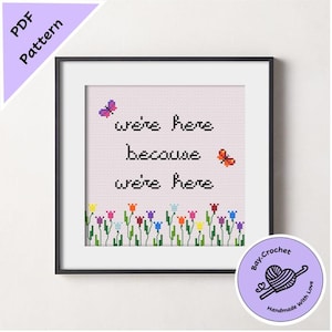 May include: Framed cross-stitch art with the text "we're here because we're here" and colorful flowers at the bottom. Two butterflies are also included in the design. The artwork is in a black frame and includes a PDF pattern.
