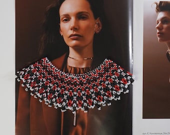 May include: A close-up of a beaded necklace with a black, white, and red pattern. The necklace is worn by a person in a magazine photo.