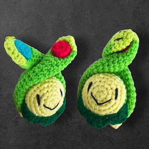 Pode incluir: Dois brinquedos de tartaruga de crochê feitos à mão. As tartarugas são principalmente verdes com barrigas amarelas e rostos sorridentes. Uma tartaruga tem uma mancha vermelha e uma mancha azul na cabeça. A outra tartaruga tem uma mancha vermelha na cabeça.