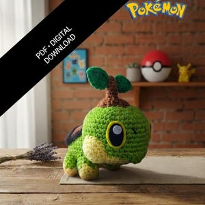 May include: A crocheted Turtwig Pokémon plushie, primarily green with yellow accents, sits on a wooden surface. The plushie has a detailed face and a small tree on its head. The background includes a brick wall, a Poké Ball, and a Pikachu figurine.