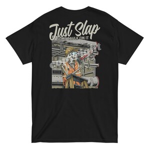 May include: Black t-shirt with a graphic of a skeleton construction worker and the text "Just Slap Some Caulk On It." The skeleton is wearing a hard hat and safety vest, holding a caulk gun. The design is set against a backdrop of pipes and machinery.