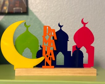 May include: A wooden base with a yellow crescent moon, green, blue, and red mosque silhouettes, and the word "RAMADAN" in orange letters.
