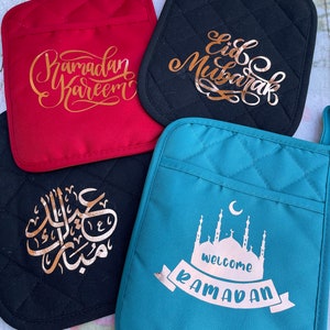May include: Four quilted pot holders with gold lettering. The pot holders feature the phrases "Ramadan Kareem", "Eid Mubarak", "Welcome Ramadan" and Arabic calligraphy.