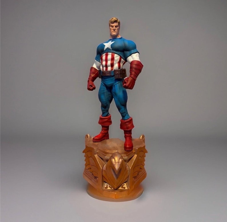 Pu&ograve; includere: Una statuetta di Captain America su una base decorativa. La figura indossa un costume blu, bianco e rosso con una stella sul petto. La base &egrave; dorata e presenta un design ornato.