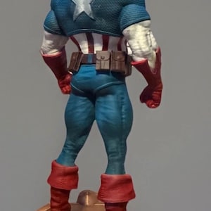 Pu&ograve; includere: Statuetta dettagliata di Captain America vista da dietro, che mostra il suo costume iconico. La figura &egrave; prevalentemente blu, rossa e bianca, con una grande stella bianca sulla schiena. Stivali e guanti sono rossi, su una base dorata.