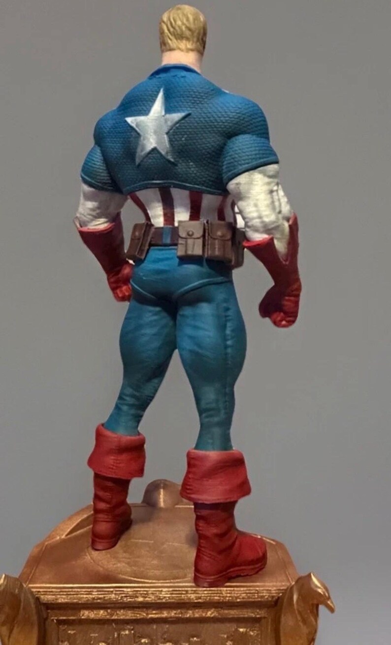 Pu&ograve; includere: Statuetta dettagliata di Captain America vista da dietro, che mostra il suo costume iconico. La figura &egrave; prevalentemente blu, rossa e bianca, con una grande stella bianca sulla schiena. Stivali e guanti sono rossi, su una base dorata.