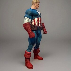 Pu&ograve; includere: Una action figure di Captain America in posa di profilo. La figura indossa una maglia blu con una stella bianca, un busto a righe rosse e bianche, pantaloni blu, stivali rossi e guanti rossi. La figura ha i capelli biondi e una cintura marrone.